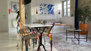 A modern living room with a dining area, featuring a large window, a sofa, a coffee table, and a potted plant. - Studio 11 bis – Facing Vichy Parks (Vichy)