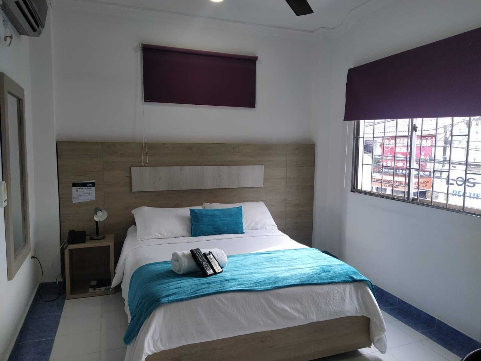 Una habitación de hotel con cama, mesita de noche, ventana que da a la calle y ventilador de techo.