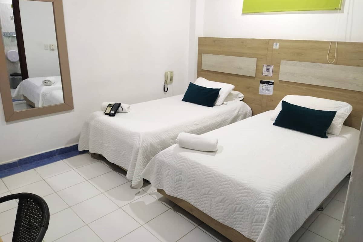 Quarto de hotel com duas camas de solteiro, um espelho, um telefone e uma parede verde.