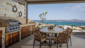 Une terrasse extérieure avec un barbecue, des chaises en osier et une vue sur la mer.