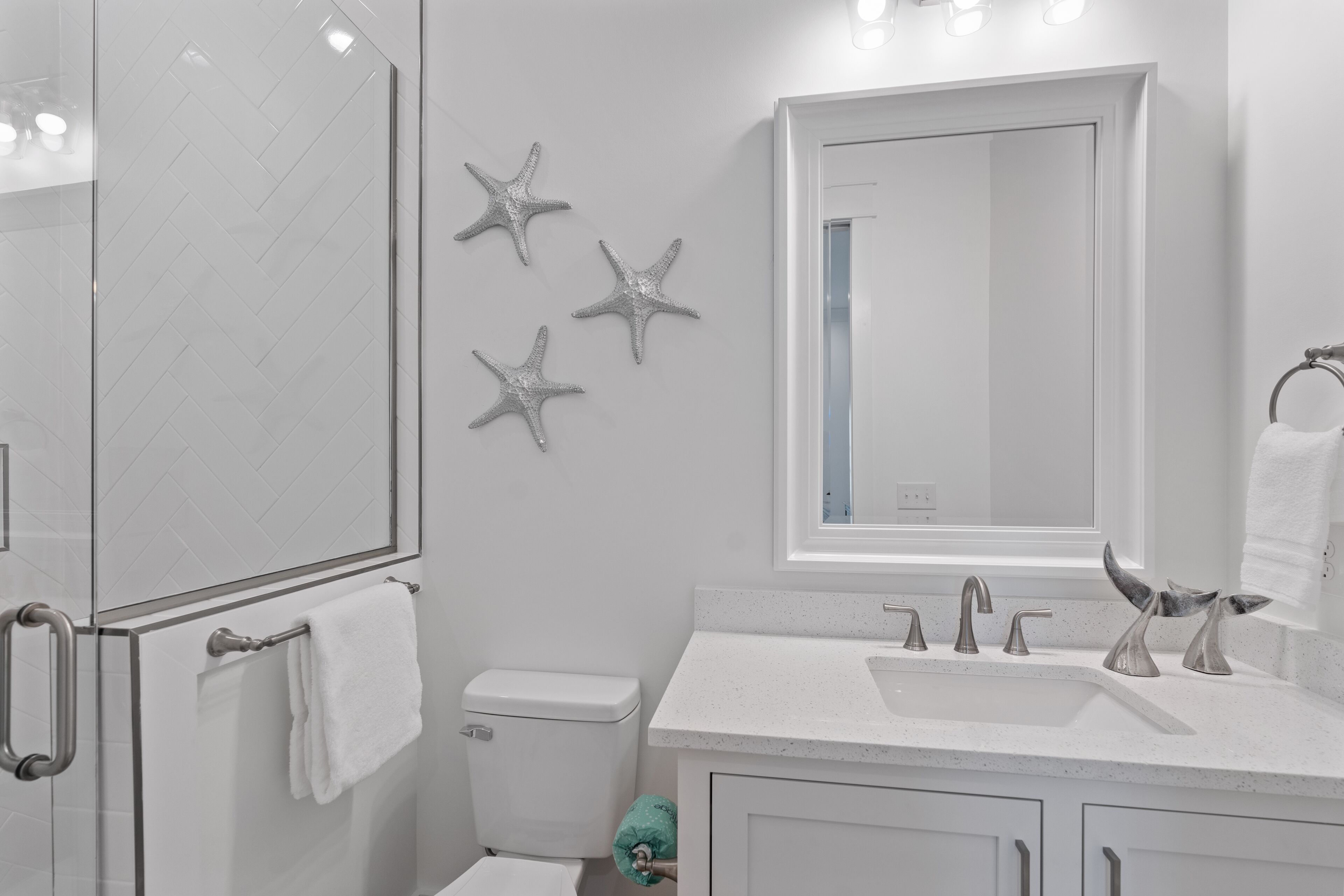 A modern bathroom with a glass shower enclosure, a toilet, a sink with a mirror above it, and decorative starfish on the wall.