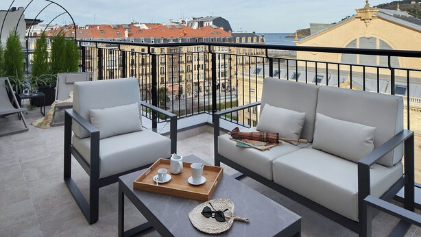 Un balcon avec un canapé, deux fauteuils, une table basse et un plateau avec des tasses et une carafe.