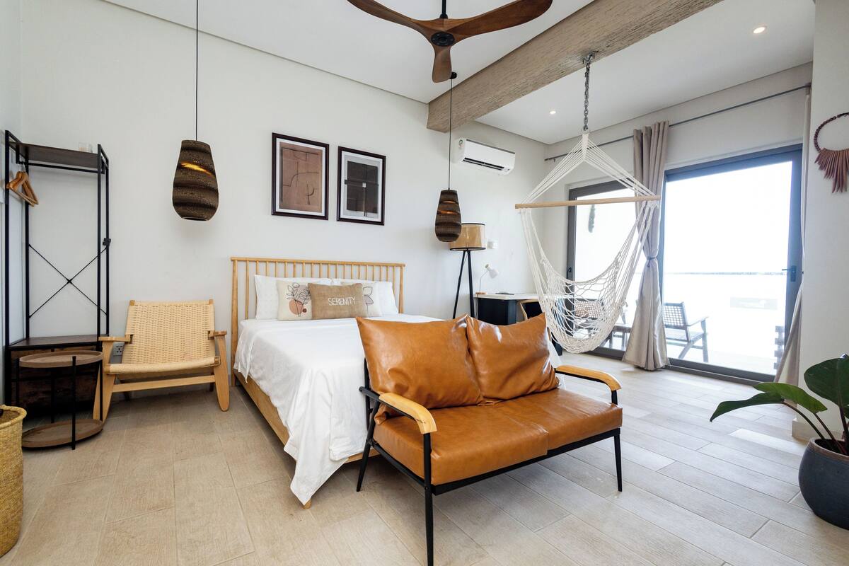 Een moderne slaapkamer met een bed, een leren bank, een hangstoel en een groot raam.