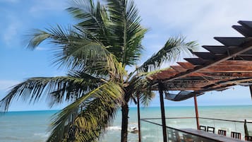 A beach view with a palm tree and a wooden pergola overlooking the ocean.