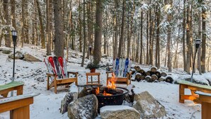 A snow-covered forest with a fire pit, skis, and benches.