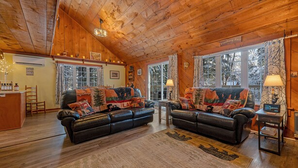 A cozy cabin interior with two leather sofas, a wooden ceiling, and large windows.
