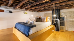 Ein Schlafzimmer mit einem Bett aus Holz, einer Hängeleuchte und einer Tür mit ornamentalem Wandpapier.