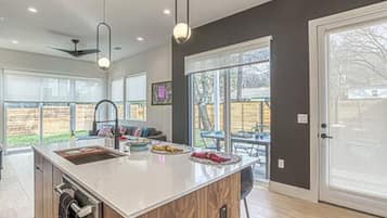 A modern kitchen with a large island, a dining area with a table and chairs, and a sliding glass door leading to a backyard.
