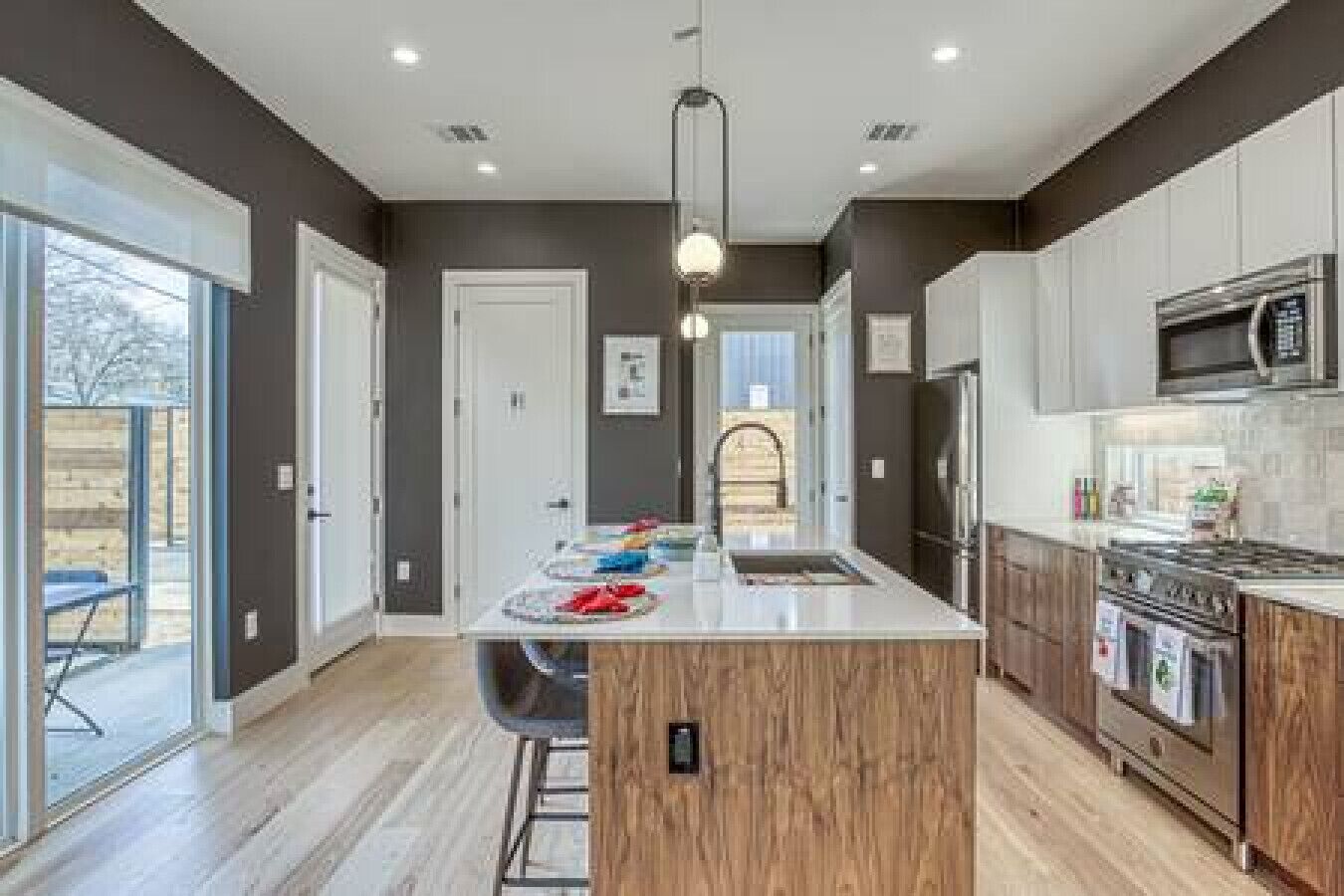 A modern kitchen with a central island, stainless steel appliances, and a view to the outside.