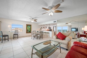 A spacious living area with a glass coffee table, a red sofa, and a dining area with chairs and a table.