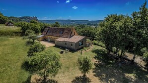 A rustic house with a tiled roof, surrounded by a grassy area and trees, with a view of hills and a castle in the distance. - Fully renovated in 2023, a typical house with pool (12x6 m) & spacious garden (Saint-Vincent-de-Cosse)