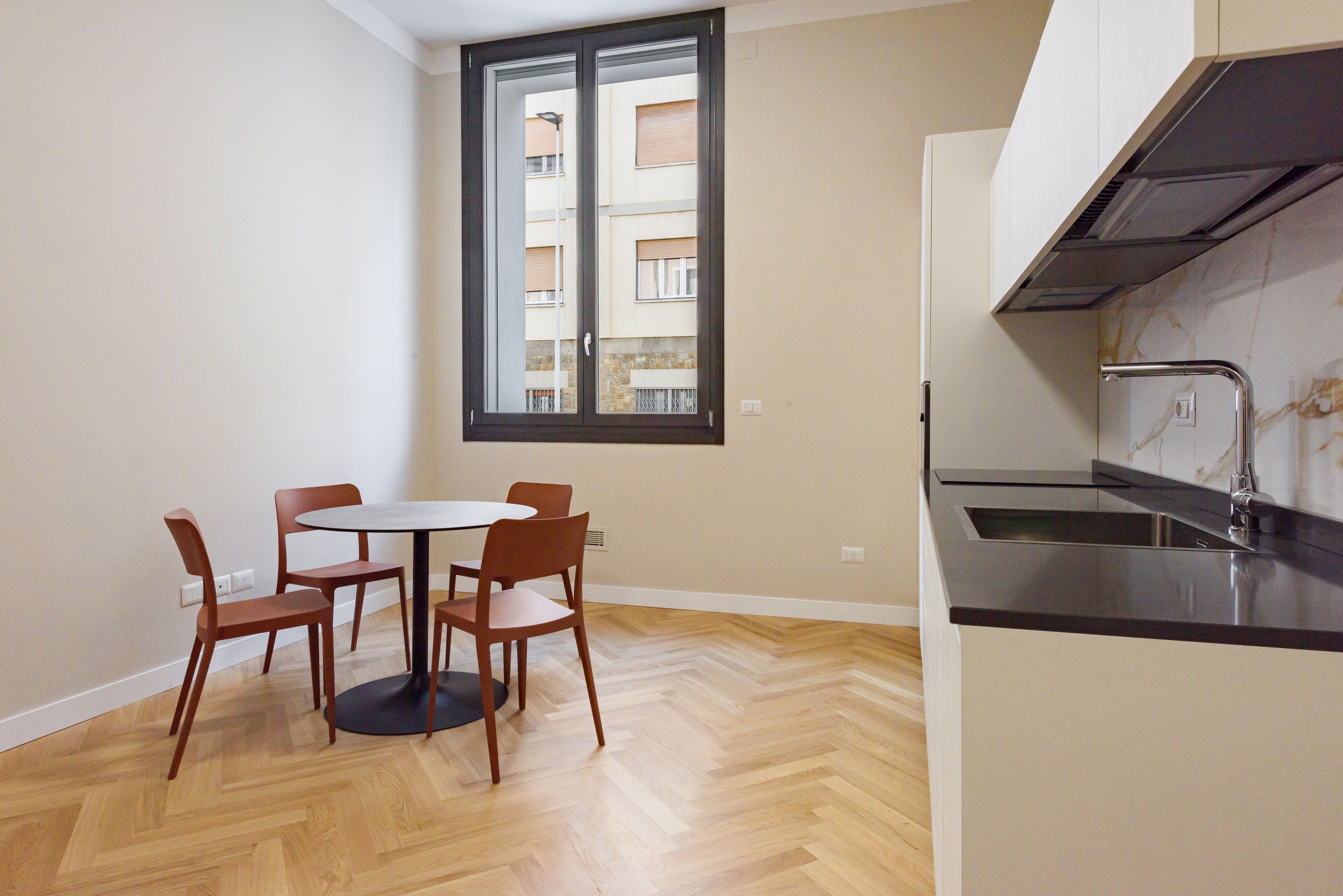 Une cuisine de taille réduite, dotée d’un plan de travail noir et d’une fenêtre donnant sur un immeuble.