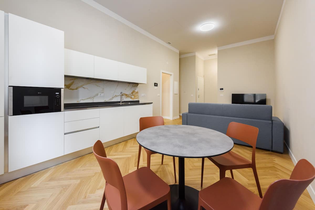 A modern kitchen with white cabinets, a built-in microwave, and a marble backsplash. There is a round table with four chairs in the center of the room.