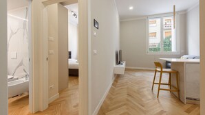 Un appartement moderne doté d’un parquet en bois disposé en chevrons, d’une cuisine avec un coin bar et d’une vue sur un immeuble à travers une grande fenêtre.