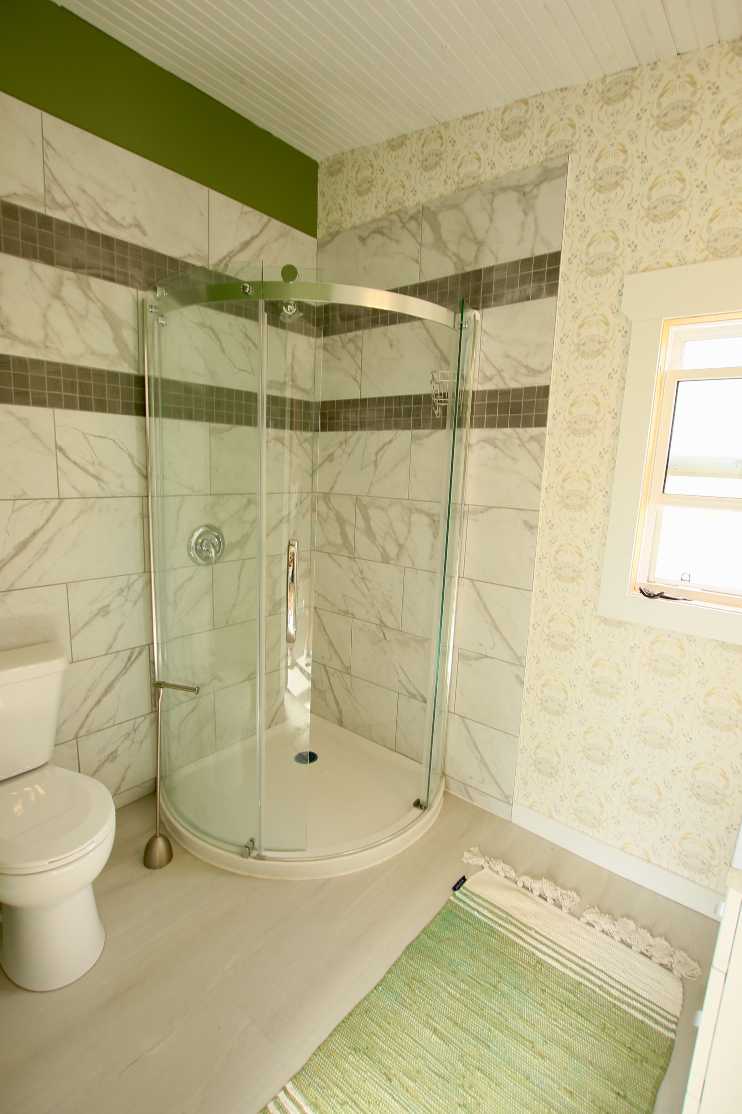 Un baño con ducha de vidrio, inodoro y pared con diseño.