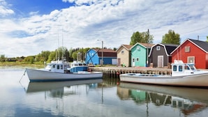 A calm waterfront with two boats docked, a row of colorful houses, and a clear sky.