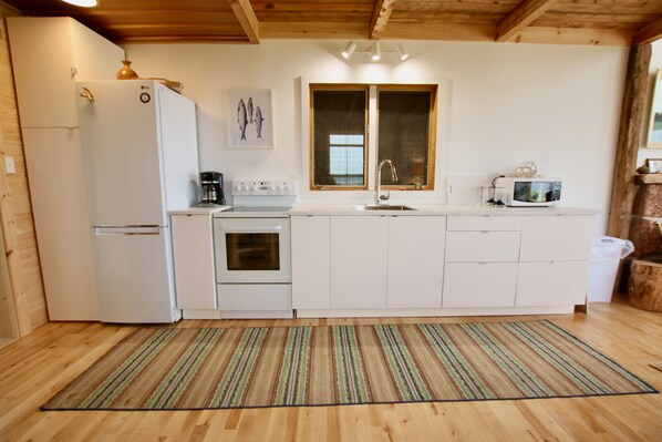 Una cocina compacta con gabinetes blancos, un refrigerador, una estufa, un lavamanos y un microondas.