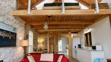 A spacious living room with a red sofa, wooden ceiling beams, and a model ship.