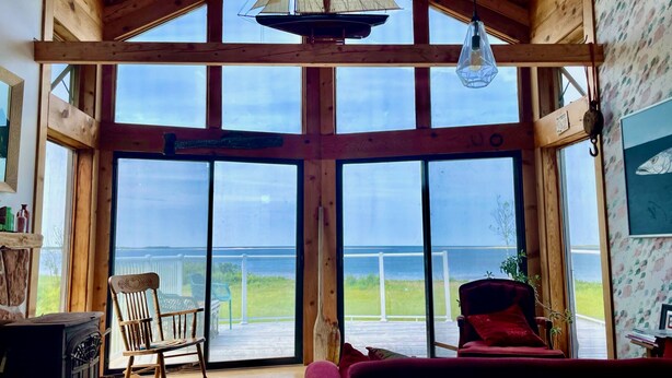 A wooden interior with large windows, a rocking chair, and a red sofa.