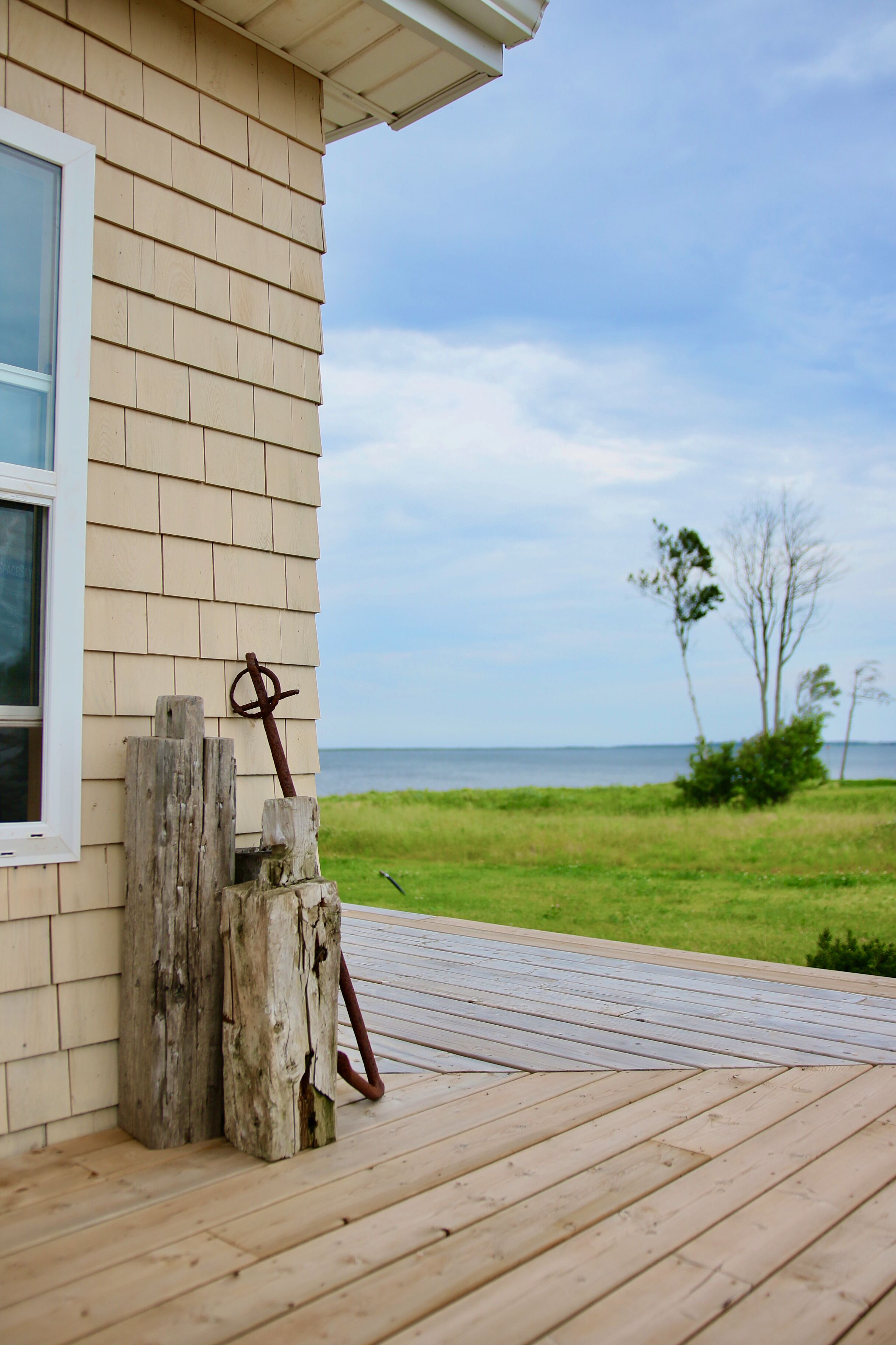A wooden deck with a rustic post and a metal tool leaning against a beige house wall.