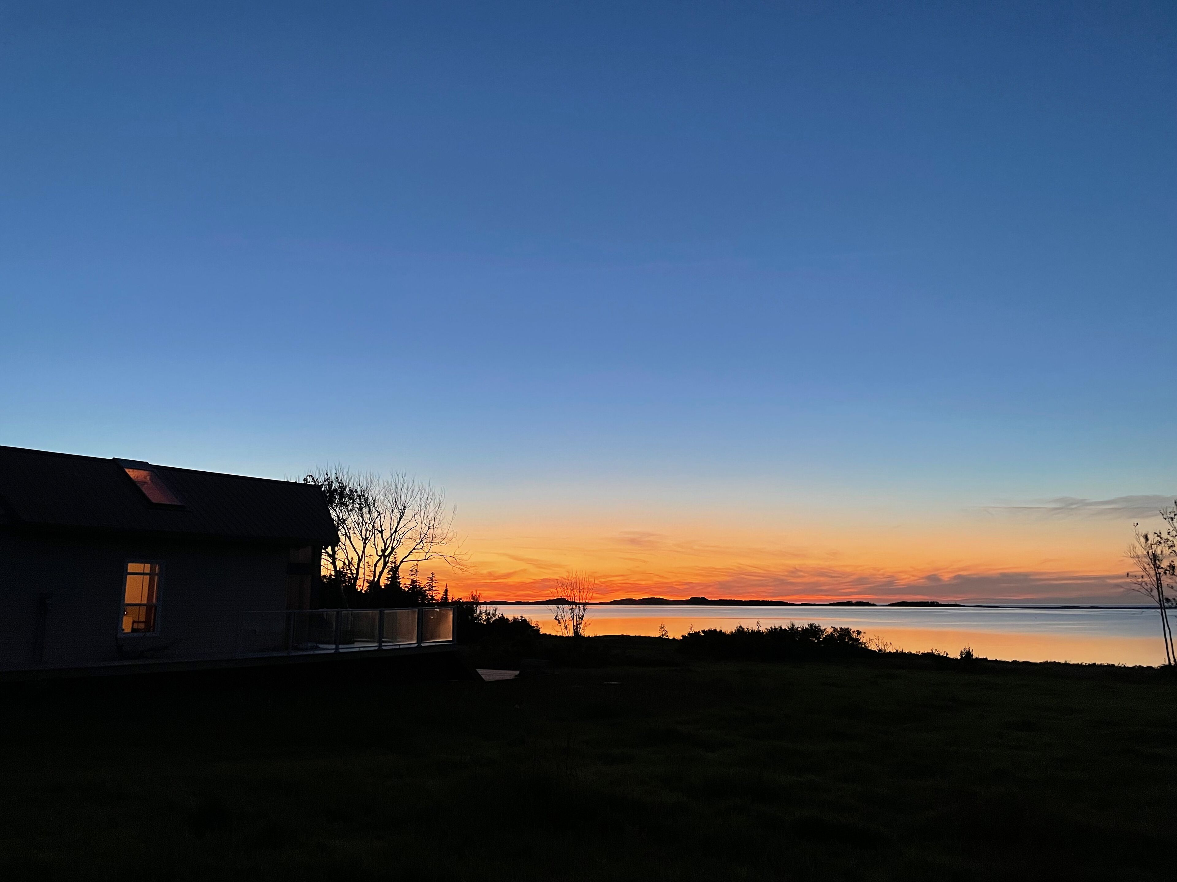 Une maison avec une fenêtre bien visible, d’où l’on peut admirer un coucher de soleil sur une étendue d’eau.