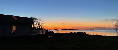 Une maison avec une fenêtre bien visible, d’où l’on peut admirer un coucher de soleil sur une étendue d’eau.