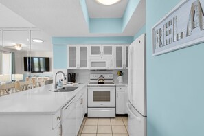 Une cuisine moderne avec des meubles blancs, un four à micro-ondes encastré et un grand îlot central doté d’un évier.