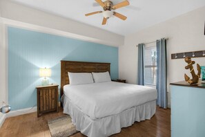 Une chambre à coucher avec un lit, une tête de lit en bois, une table de chevet, une lampe et un ventilateur de plafond.