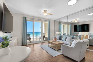 Un vaste espace de vie comprenant un canapé, une table basse et un téléviseur. Un balcon offre une vue sur l’océan.