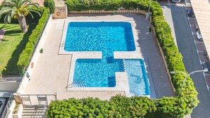 An aerial view of a swimming pool surrounded by greenery, with a clear sky above.