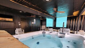 A hot tub area with a ceiling fan, wooden flooring, and a view of the outdoors.