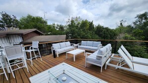 A wooden deck with white outdoor furniture, including sofas and chairs, and a glass-top table with candles.