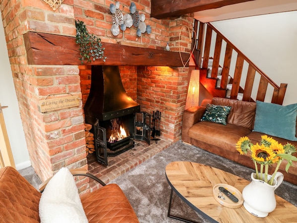 Una sala de estar acogedora con una chimenea de ladrillo, un sofá de cuero y una mesa de centro con un jarrón de girasoles.