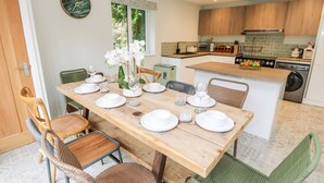 Una cocina moderna con armarios de madera, una zona de comedor con mesa de madera dispuesta para cuatro personas y una silla verde.