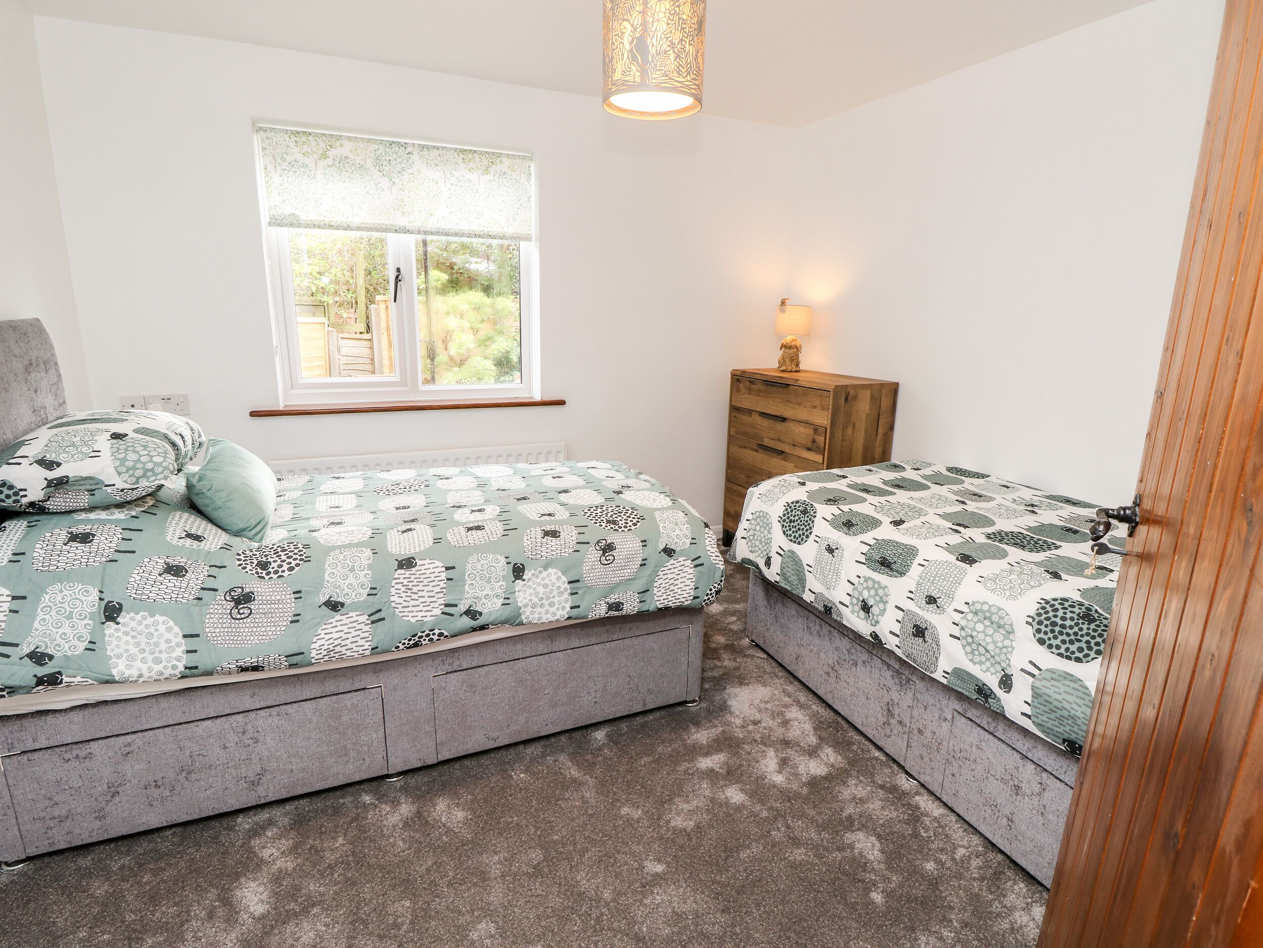 A bedroom with two beds, a window, a dresser, and a lamp.
