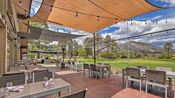 Ein Terrassenbereich im Freien mit Tischen und Stühlen, beschattet durch große Markisen, mit Blick auf einen Golfplatz und einen Berg im Hintergrund.