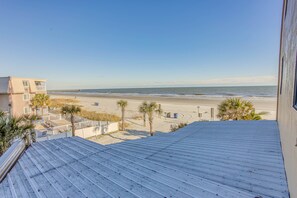 Vista de una playa desde un edificio con techo de metal, palmeras y un muelle distante.