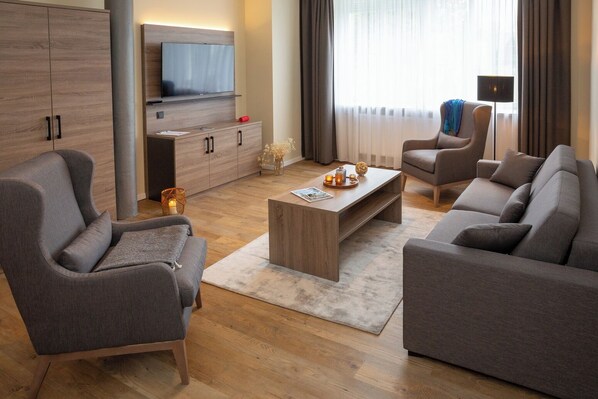 A modern living room with a sofa, armchairs, a coffee table, and a TV mounted on a wooden cabinet.