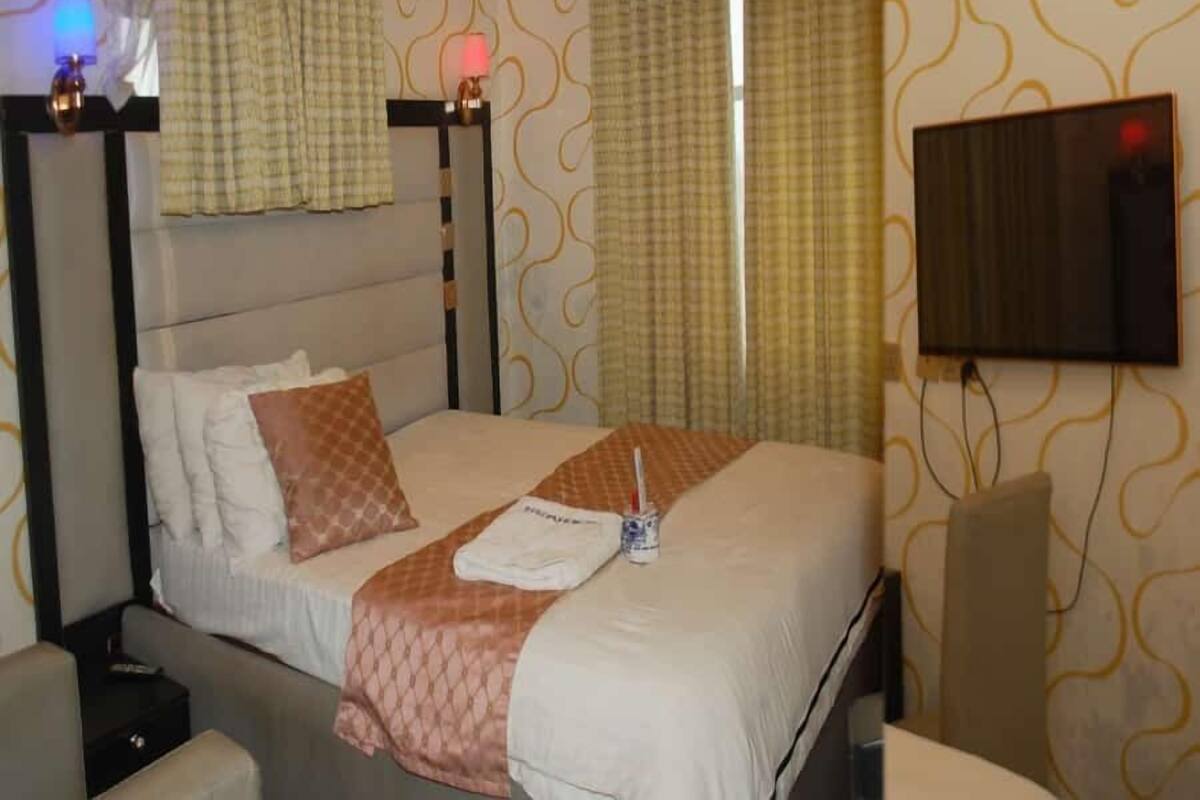 A hotel room with a bed, curtains, a TV, and a bedside lamp.