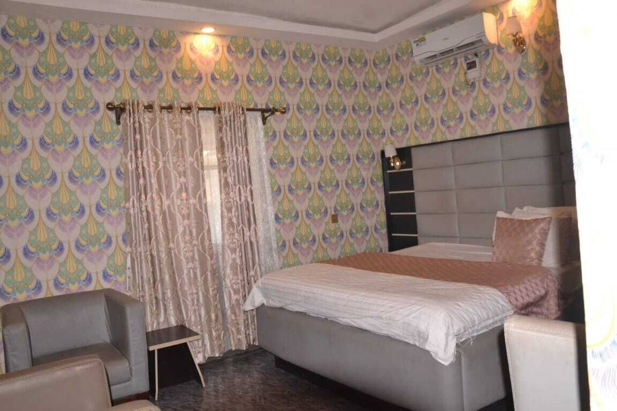 A hotel room with a bed, a chair, a small table, and patterned wallpaper.