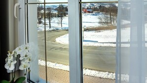 Ett fönster med utsikt över ett snöigt landskap, en röd lada och en korg av rotting med en växt i.