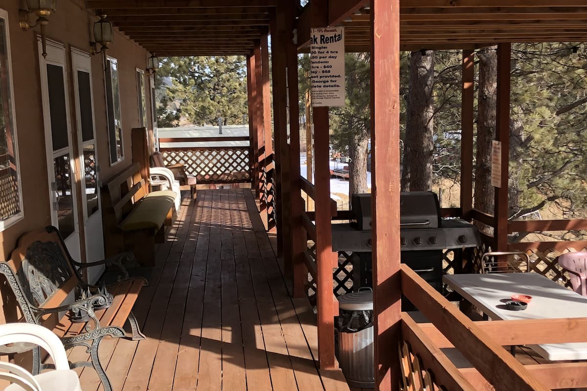 Terraza de madera con mobiliario exterior, una parrilla y un cartel que indica las tarifas de alquiler.