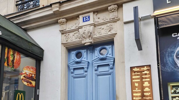 Eine blaue Tür mit der Nummer 13 darüber, ein McDonald's Schild auf der linken Seite und ein Schild mit verschiedenen Markennamen auf der rechten Seite.