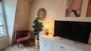 A modern living room with a flat-screen TV, a red chair, a potted plant, and a wall-mounted mirror. - Wagram Arc de Triomphe les Champs Elysées (paris)
