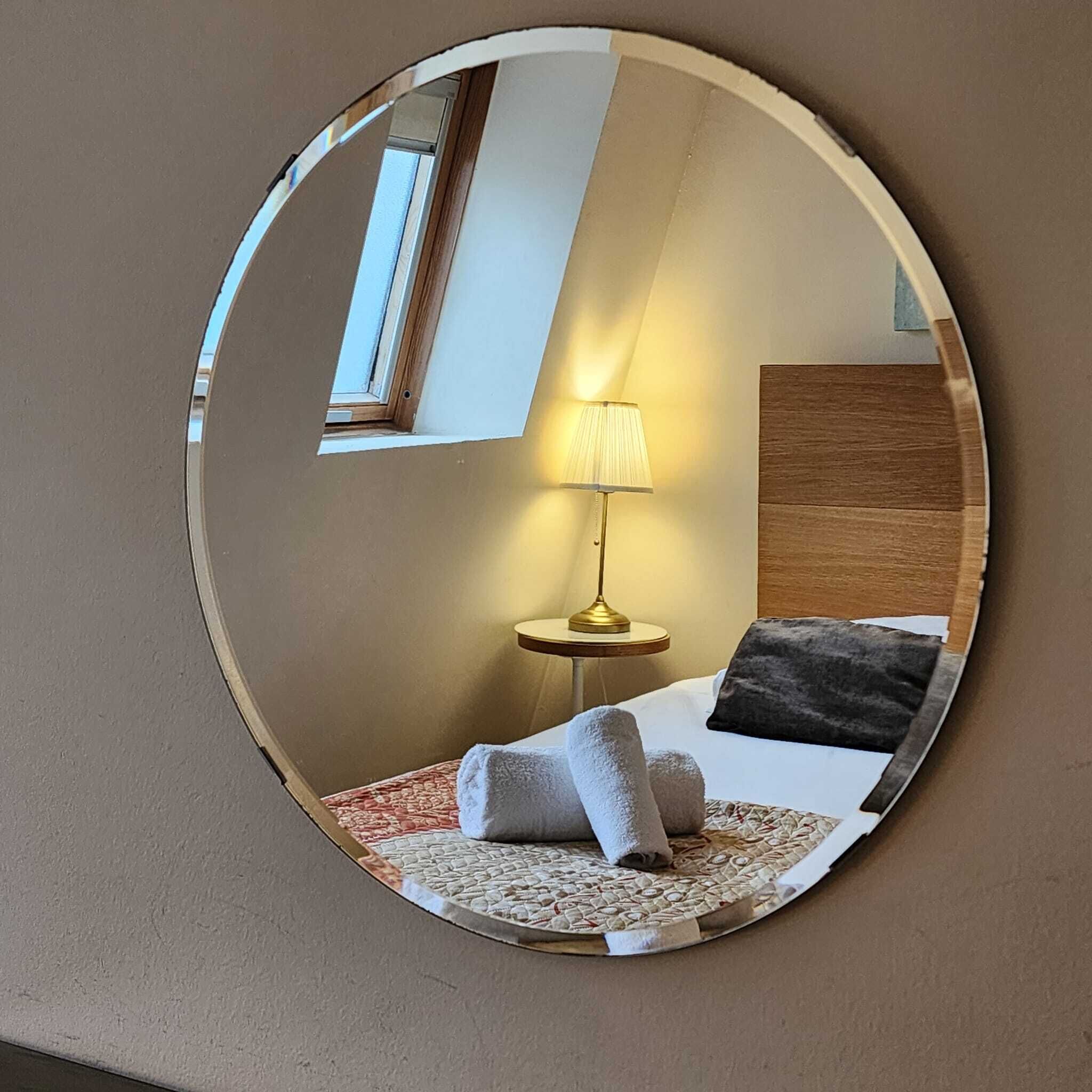 Uno specchio circolare che riflette una camera da letto con un letto, una lampada da comodino e una finestra.