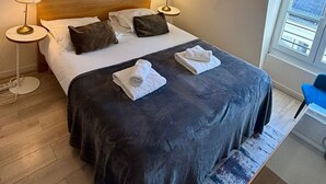 Ein Hotelzimmer mit einem großen Bett, zwei Nachttischlampen, einem Bild an der Wand, einem Fenster und einem blauen Sessel.