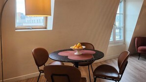 Ein Essbereich mit einem runden Tisch, vier Stühlen, einer Stehlampe und einem Fenster mit Blick auf Gebäude.