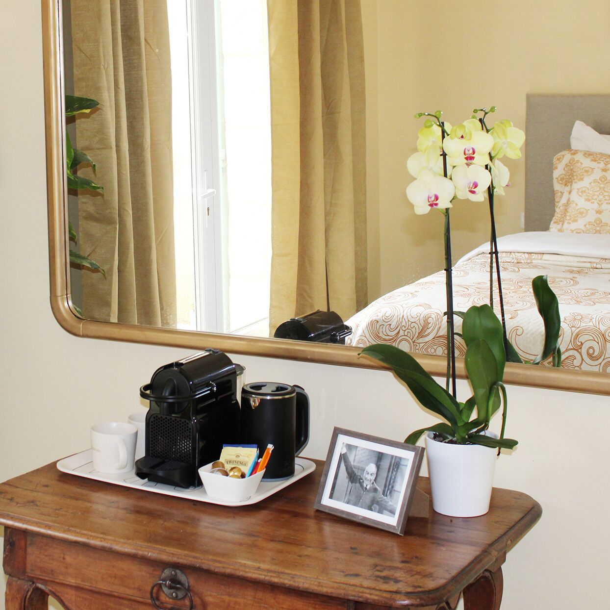 Un bureau en bois avec une machine à café, des tasses, un cadre photo et une orchidée en pot.