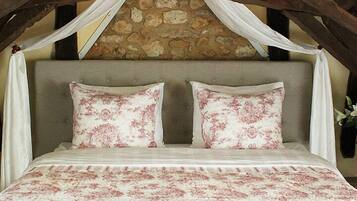 A bed with a floral bedspread and two matching pillows, a stone wall behind, and a wooden ceiling structure.