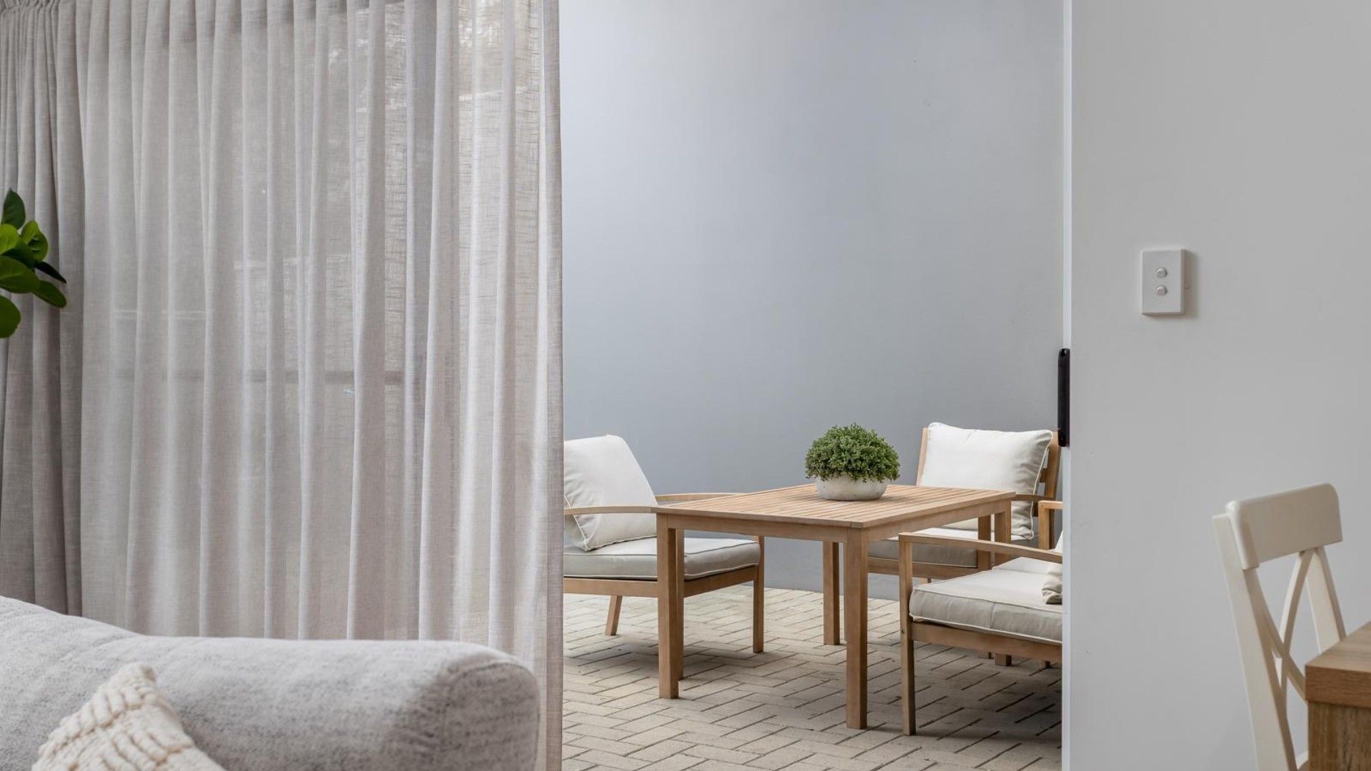 Una habitación con una mesa de madera, dos sillas, una planta en maceta y un sofá blanco.